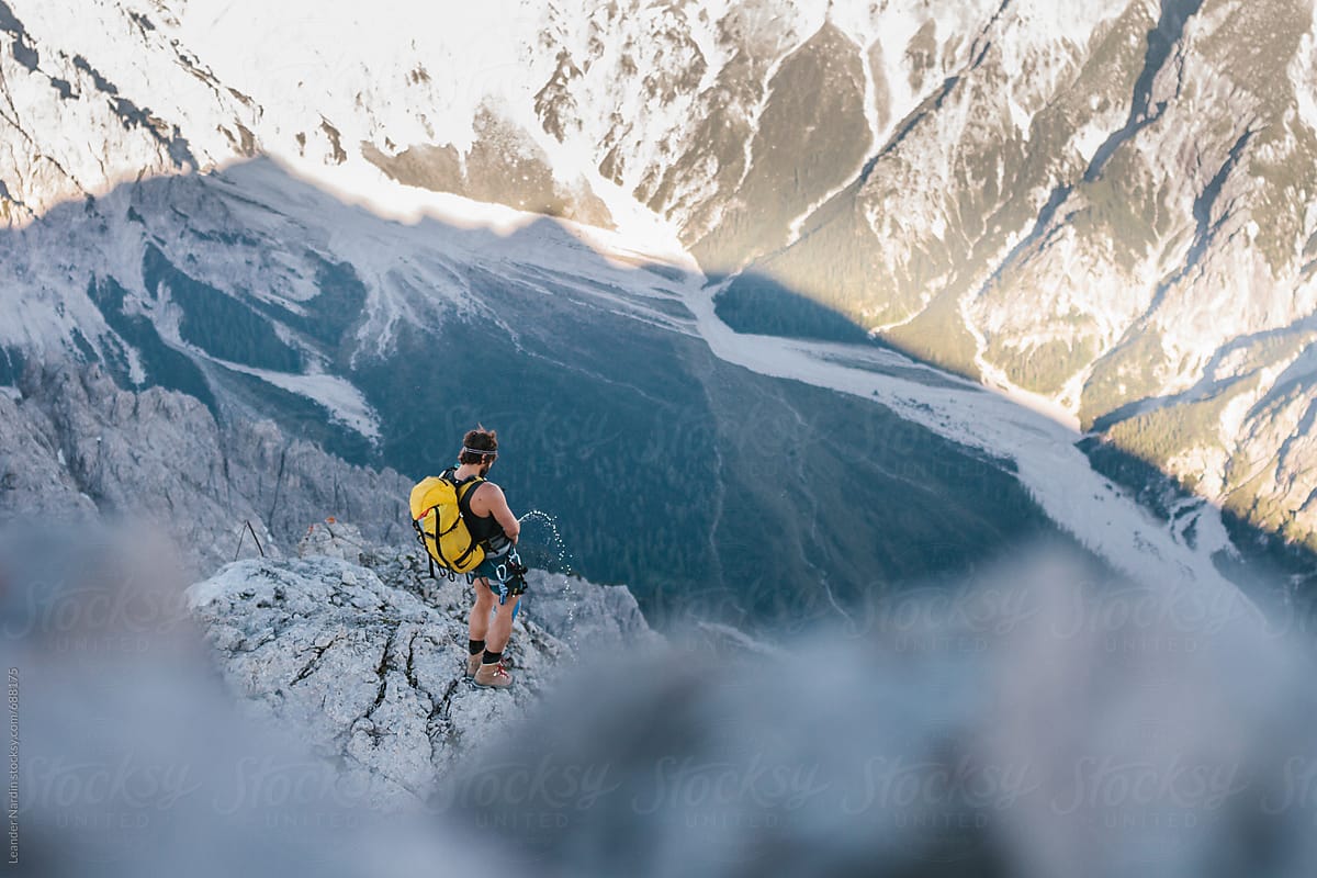 male-climber-peeing-at-the-edge-down-the-mountain-by-stocksy