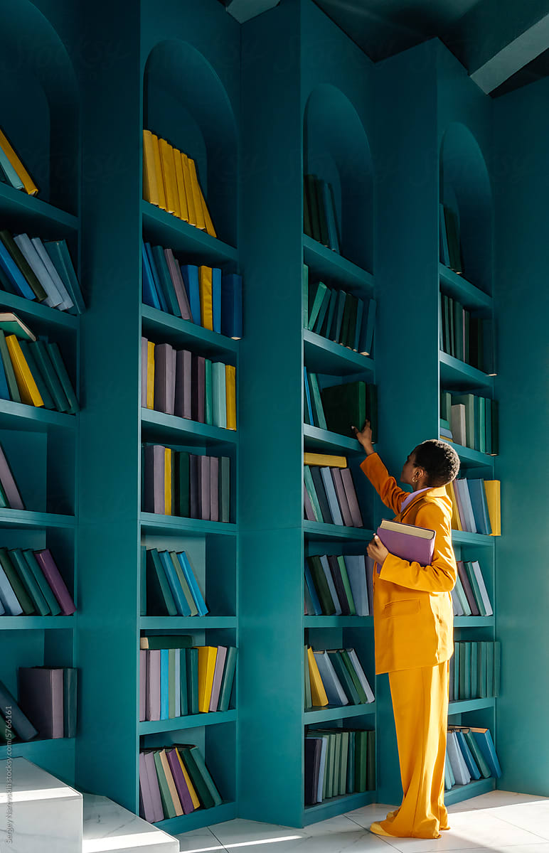 Woman in yellow suit picking books in library
