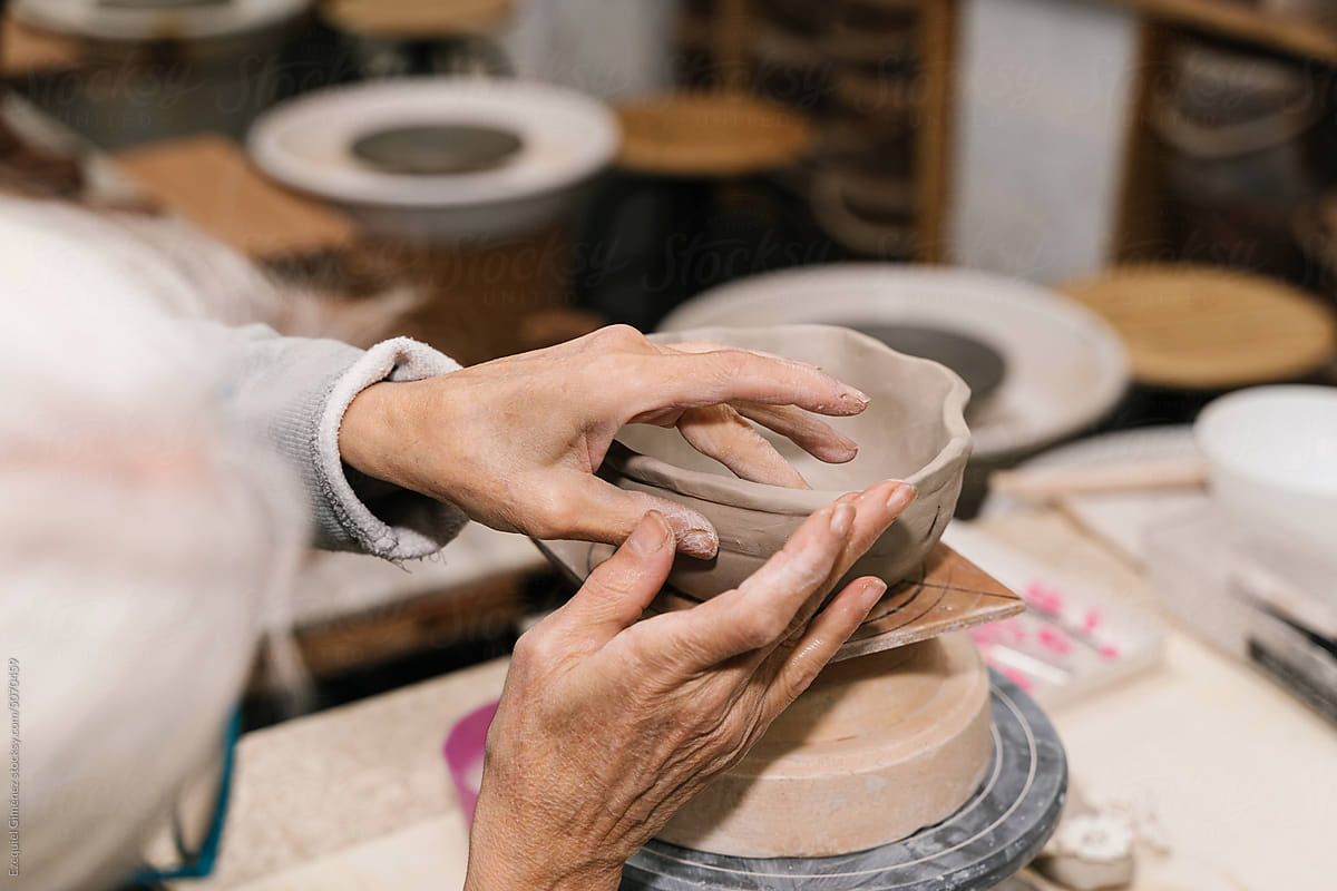 Crop elderly woman creating clay bowl in pottery
