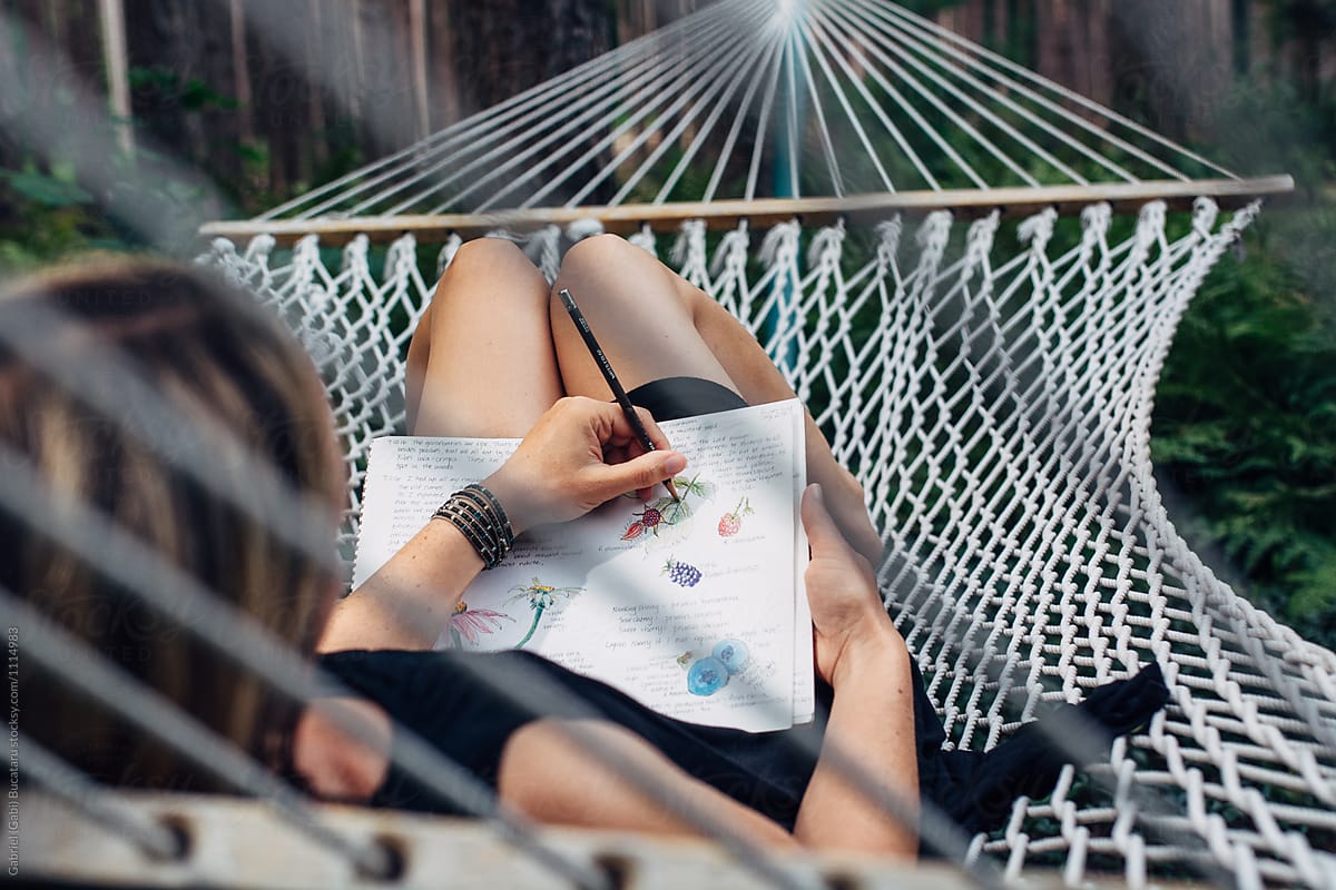 Woman laying on a hammock drawing in her nature journal