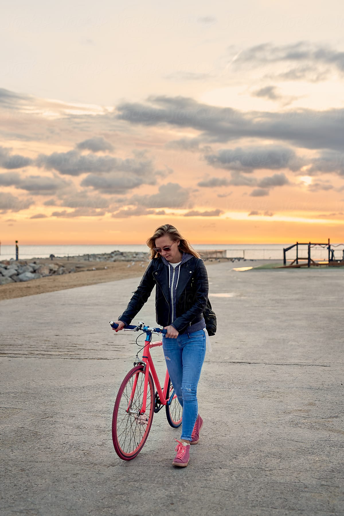 Woman walking with bicycle against sunrise at sea.
