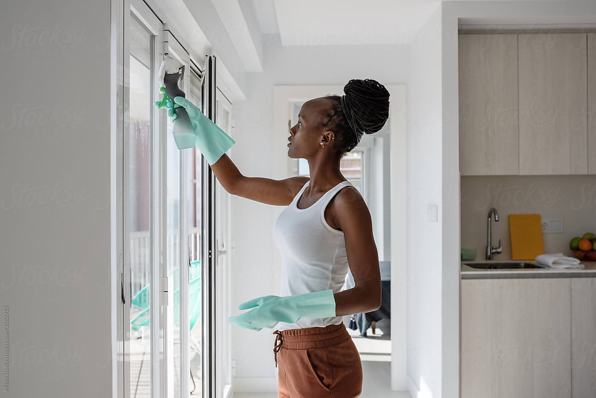 African housewife spraying detergent on kitchen window