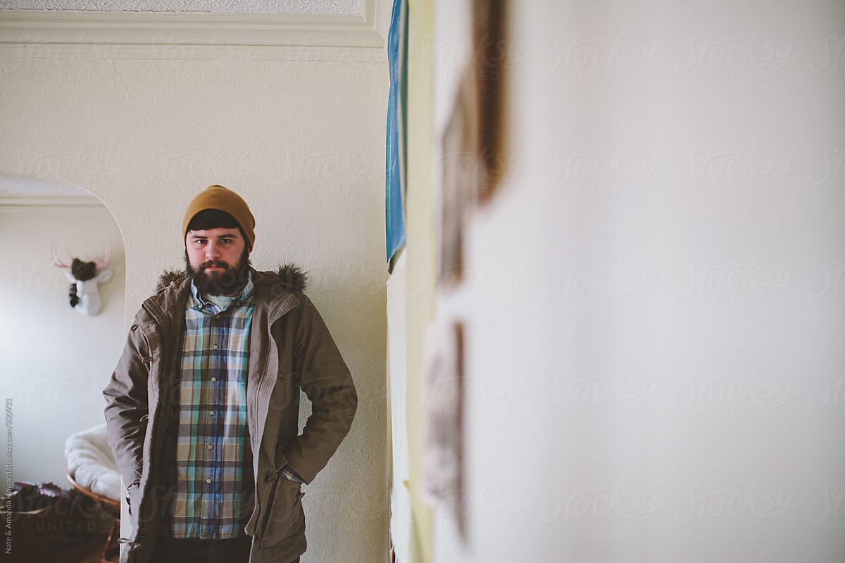man plaid shirt & jacket in the corner of a white simple home.