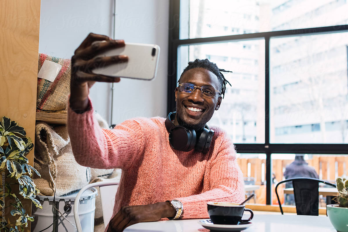 Cheerful black man taking selfie in cafe