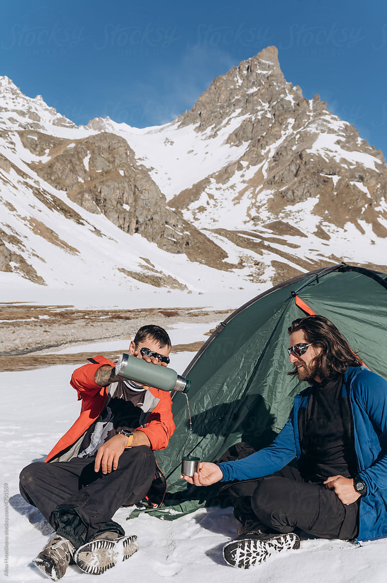 Men with hot drink in thermos in snowy mountains