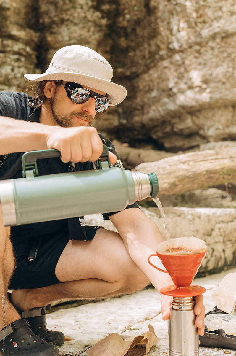 Male tourist brewing coffee near cliff