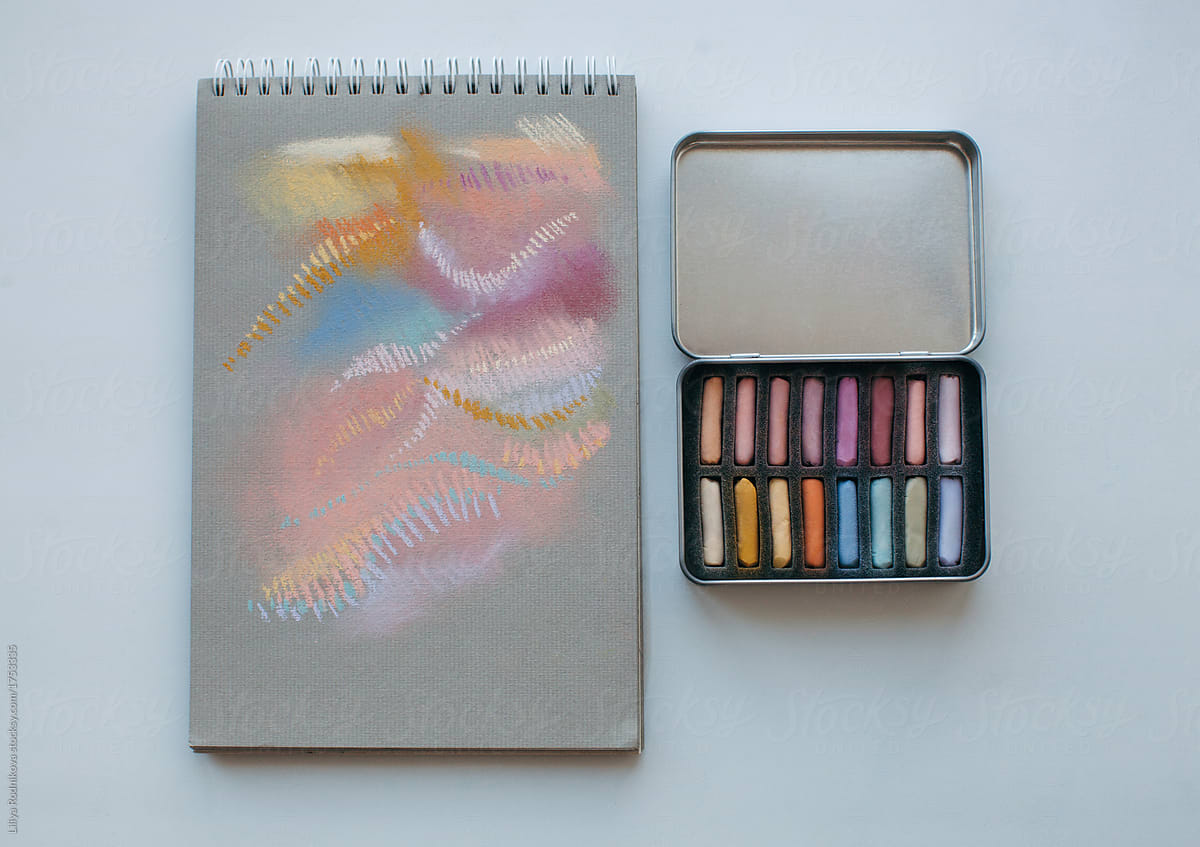 Metal box with assorted soft pastels and notebook with abstract drawing made with it
