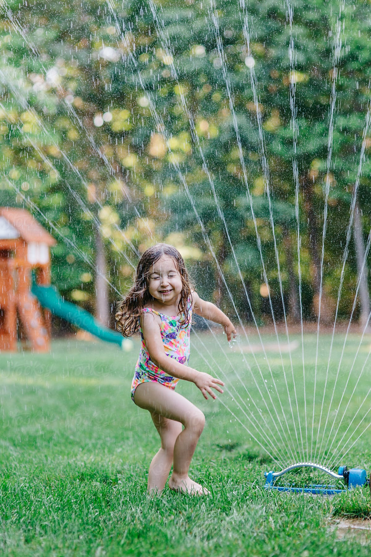 Cute toddler playing with a sprinkler in a yard