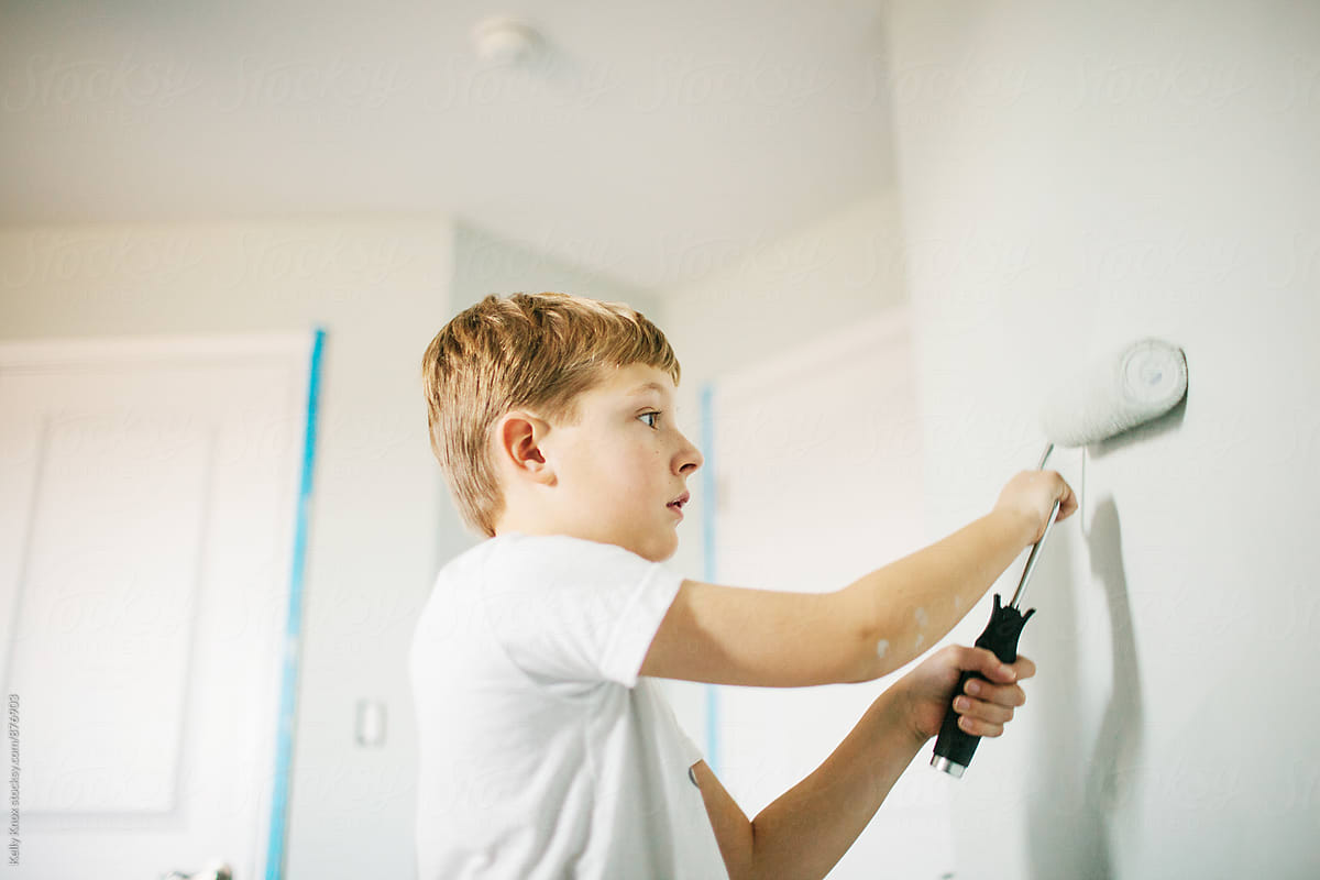 boy using a paint roller to paint a room