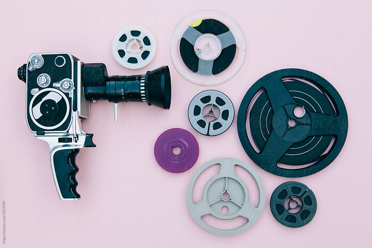 Vintage cinema camera and reels over pink background