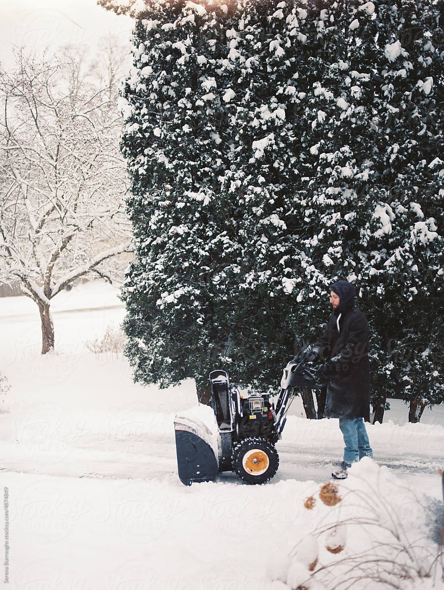 man clearing heavy snow in winter in his driveway with a snowblower