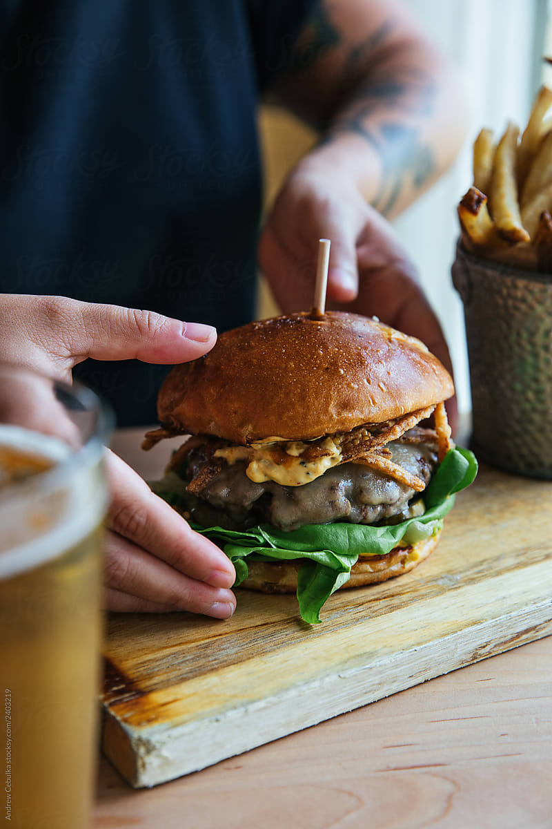 Hand Holding Cheeseburger with Fried Onions and French Fries and a Beer