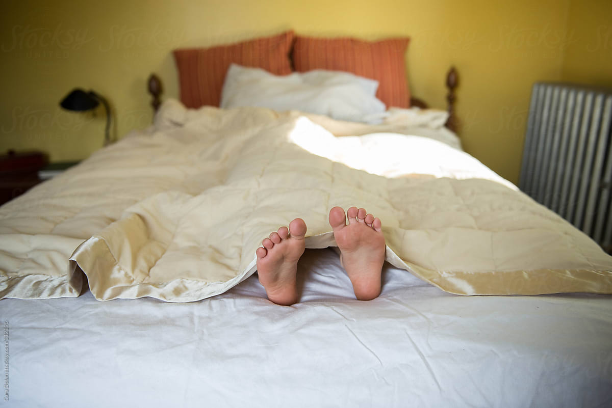The feet of a child stick out from under the covers of his bed