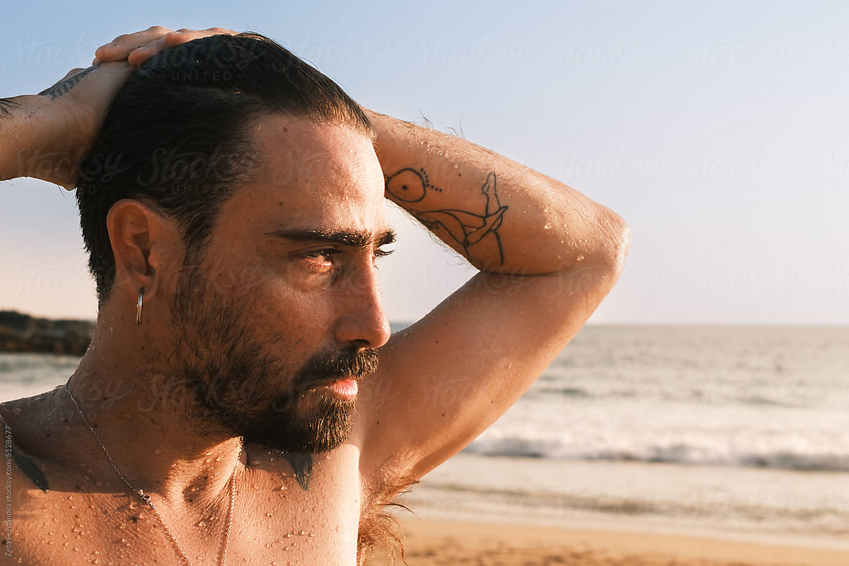 man with tattooed curls wet after a swim at a beach