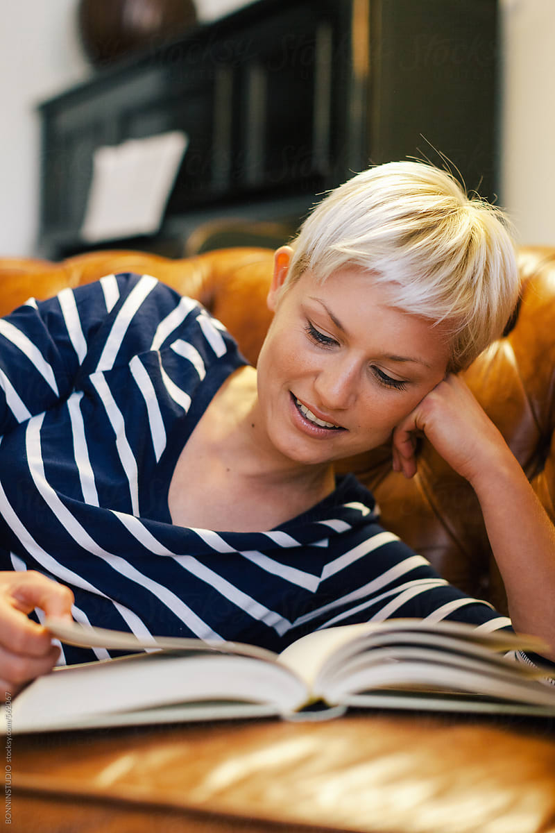 Beautiful blonde woman reading a book on the couch at home.