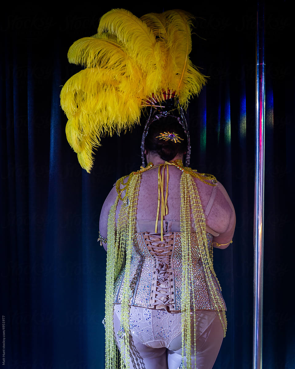 Drag queen in burlesque attire waits behind a curtain to go on stage