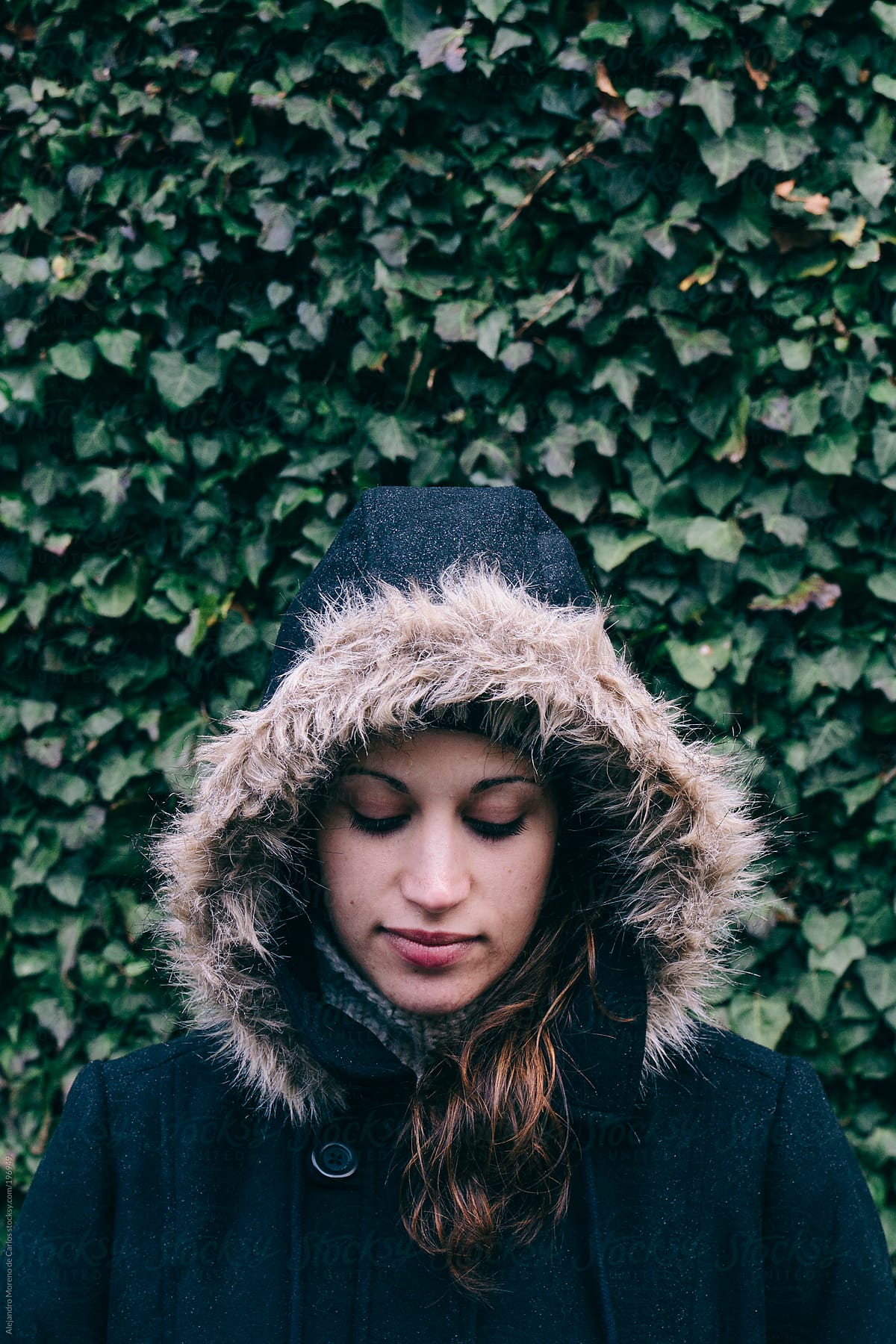 Fashion portrait of young woman wearing a parka coat and a fur hood on ivy green background