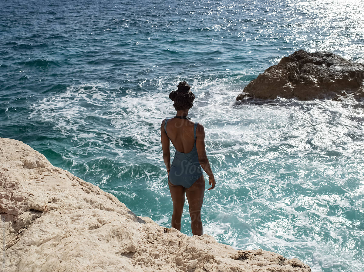 Black tourist standing on rock near waving sea