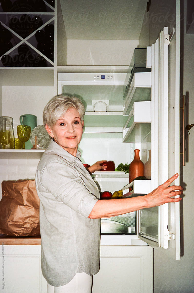 Smiling senior woman putting food in fridge, film ugc