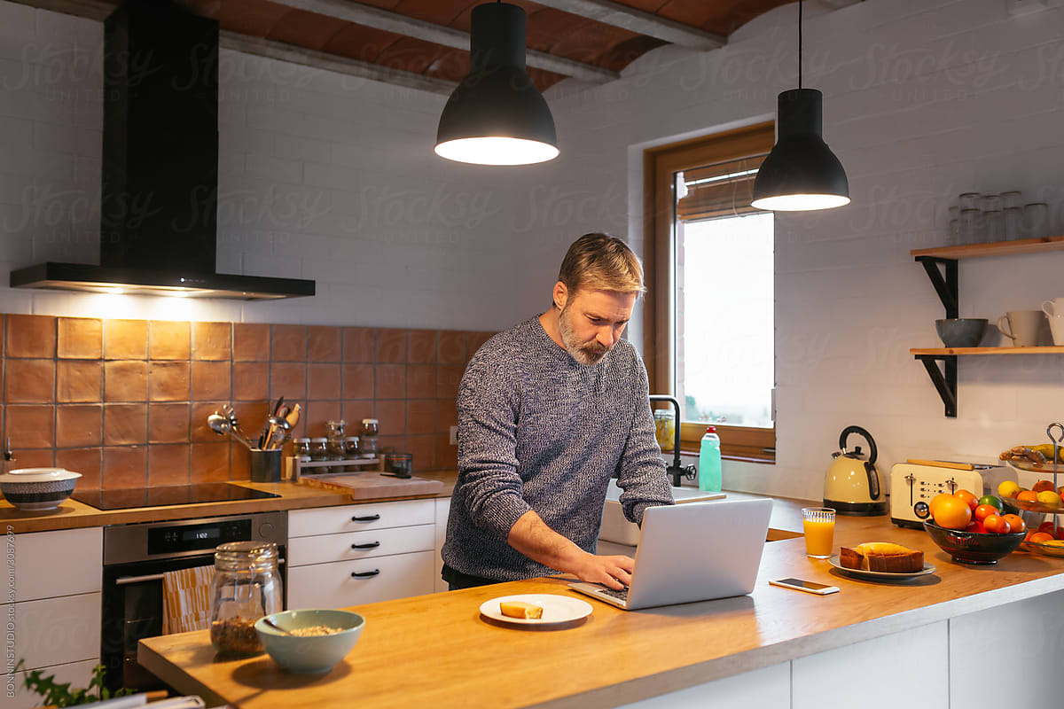 Adult man using laptop while eating in the kitchen.