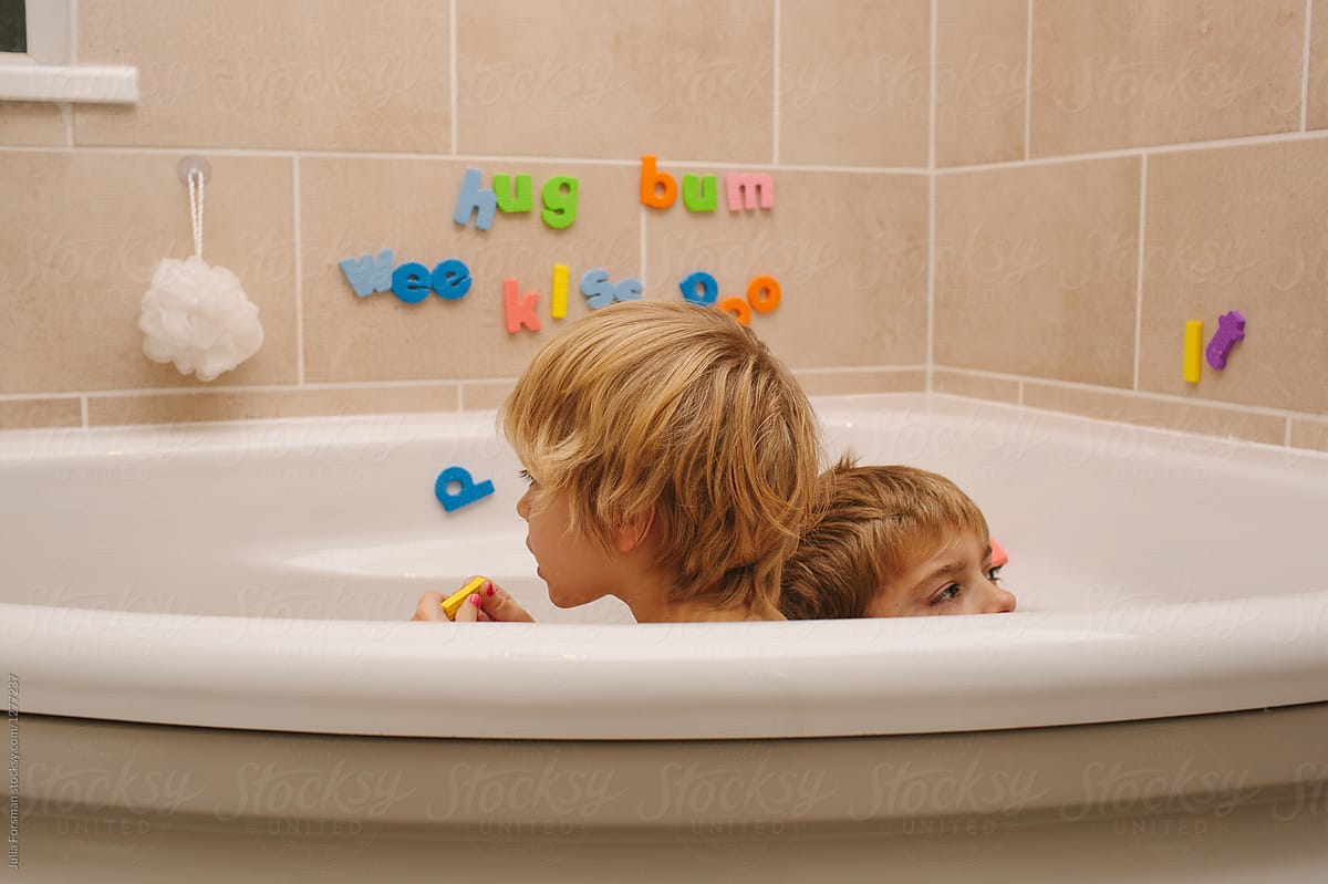Two children playing with foam letters in the bath.