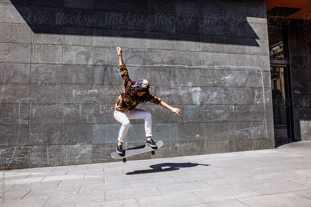 Young skater woman jumping with her skateboard in front dirty wall.