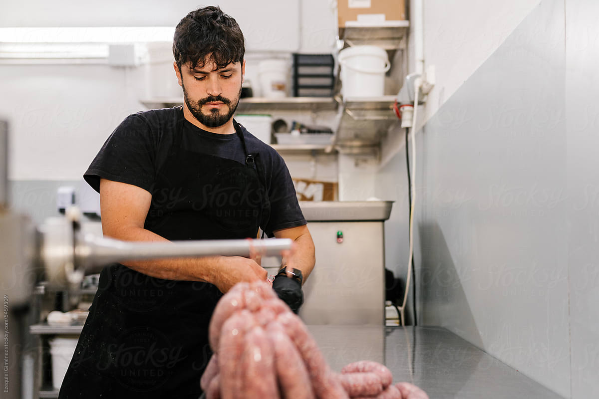 Concentrated man tying thread while making sausages