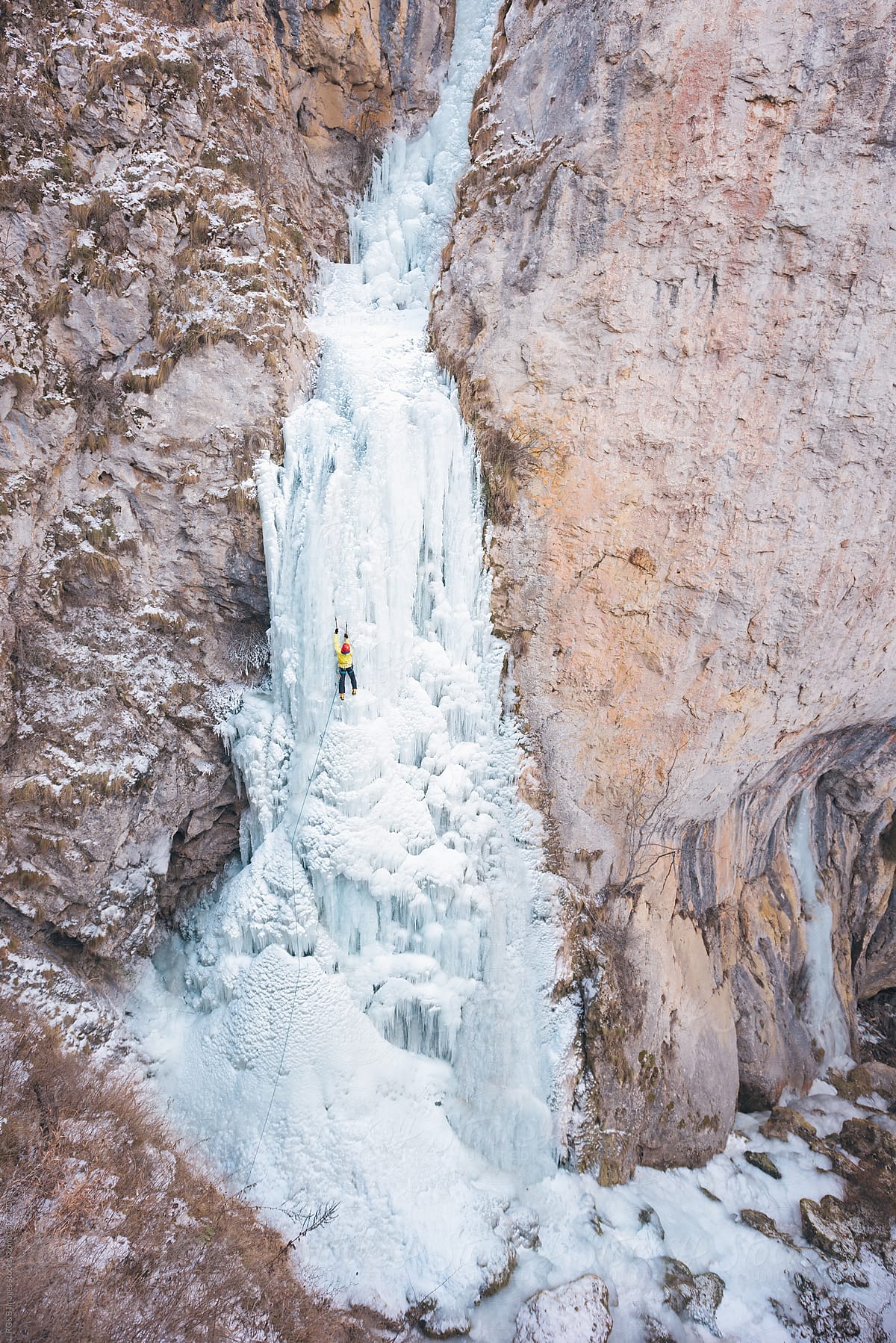 Alpinist ice climbing on frozen waterfall