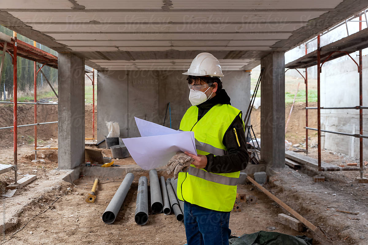 Construction engineer in protective mask examining blueprints