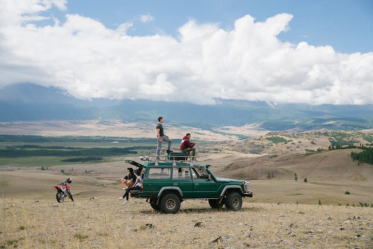 Company of young people resting on the old  jeep parked in wild mountainous area
