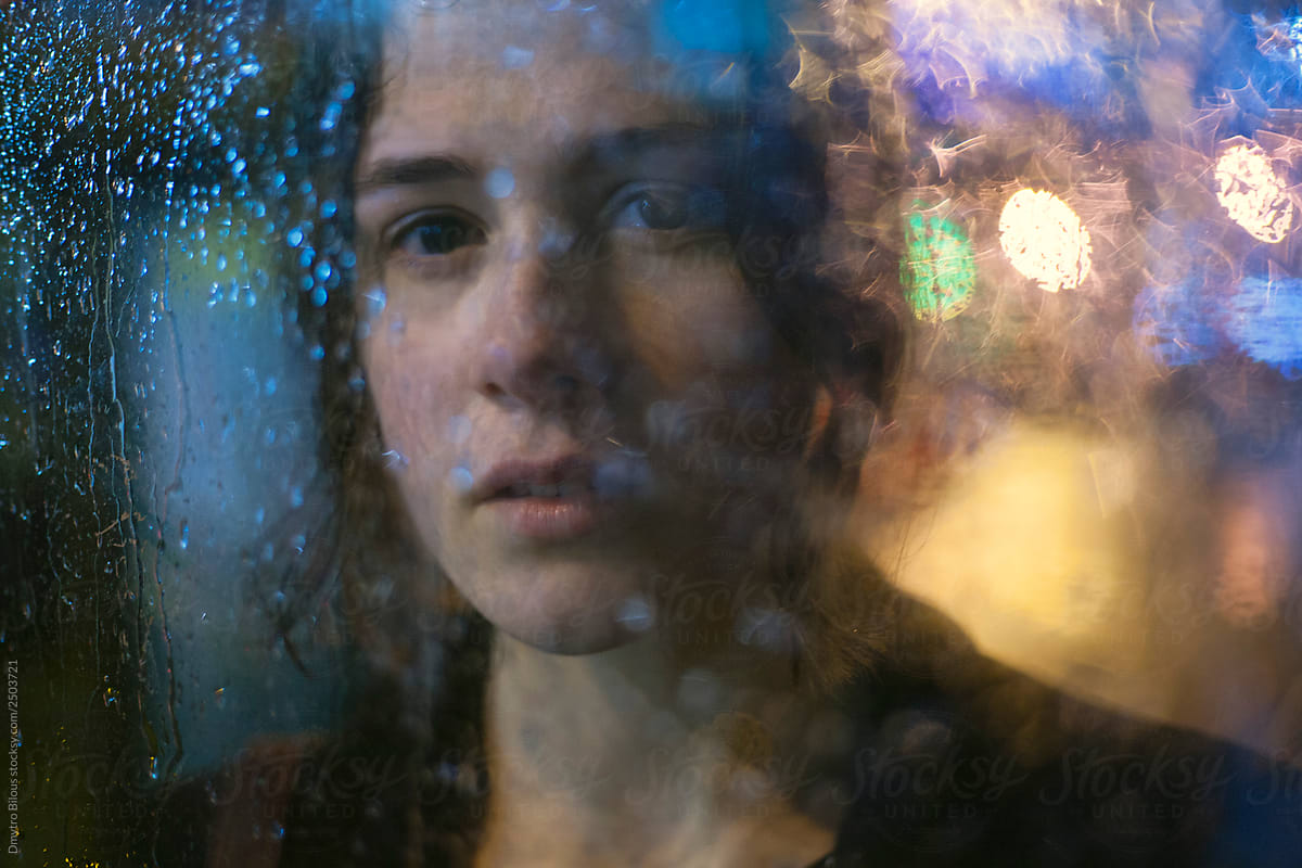 portrait of a girl through the glass with raindrops on it and beautiful bokeh during the rain