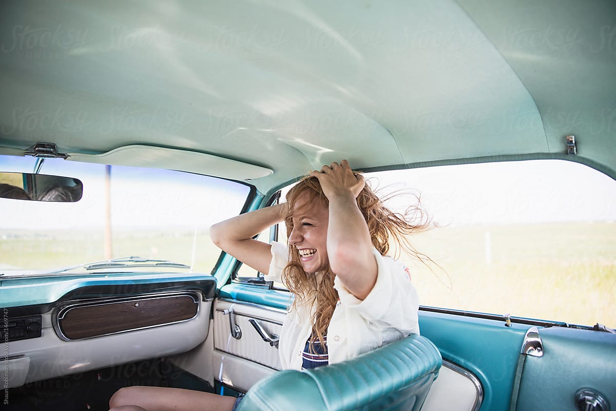 A young woman in a car with her hands in her hair smiling