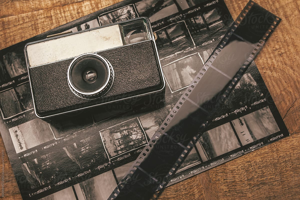 Old analog camera, film and contact sheet over wooden table.