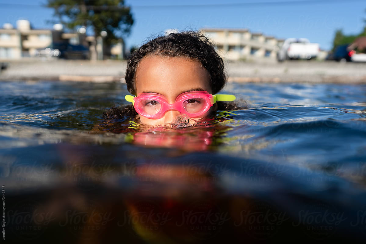 Young girl in pink goggles sinks up to her nose in ocean