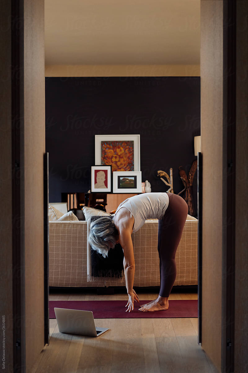Anonymous mature woman doing Ardha Uttanasana yoga pose during online training at home