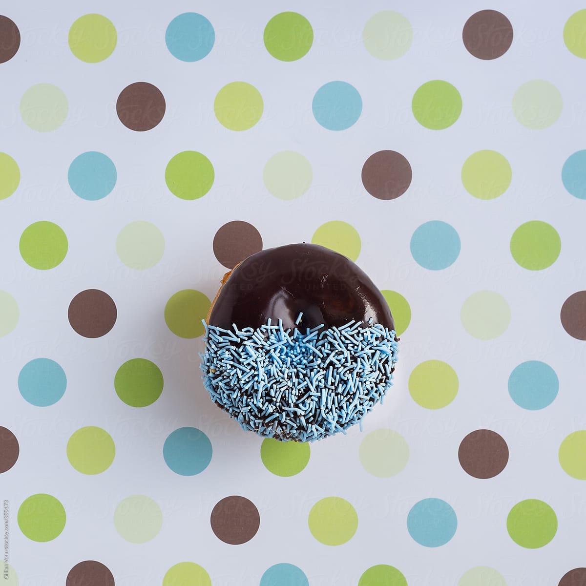 donut with chocolate icing and blue sprinkles on dotty background
