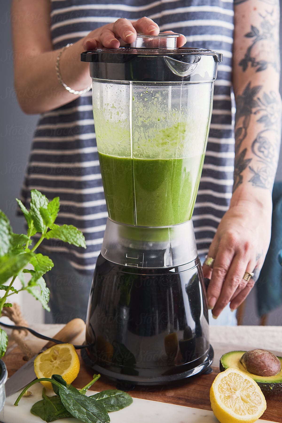 Woman with tattoos preparing a healthy detox smoothie drink in a blender.
