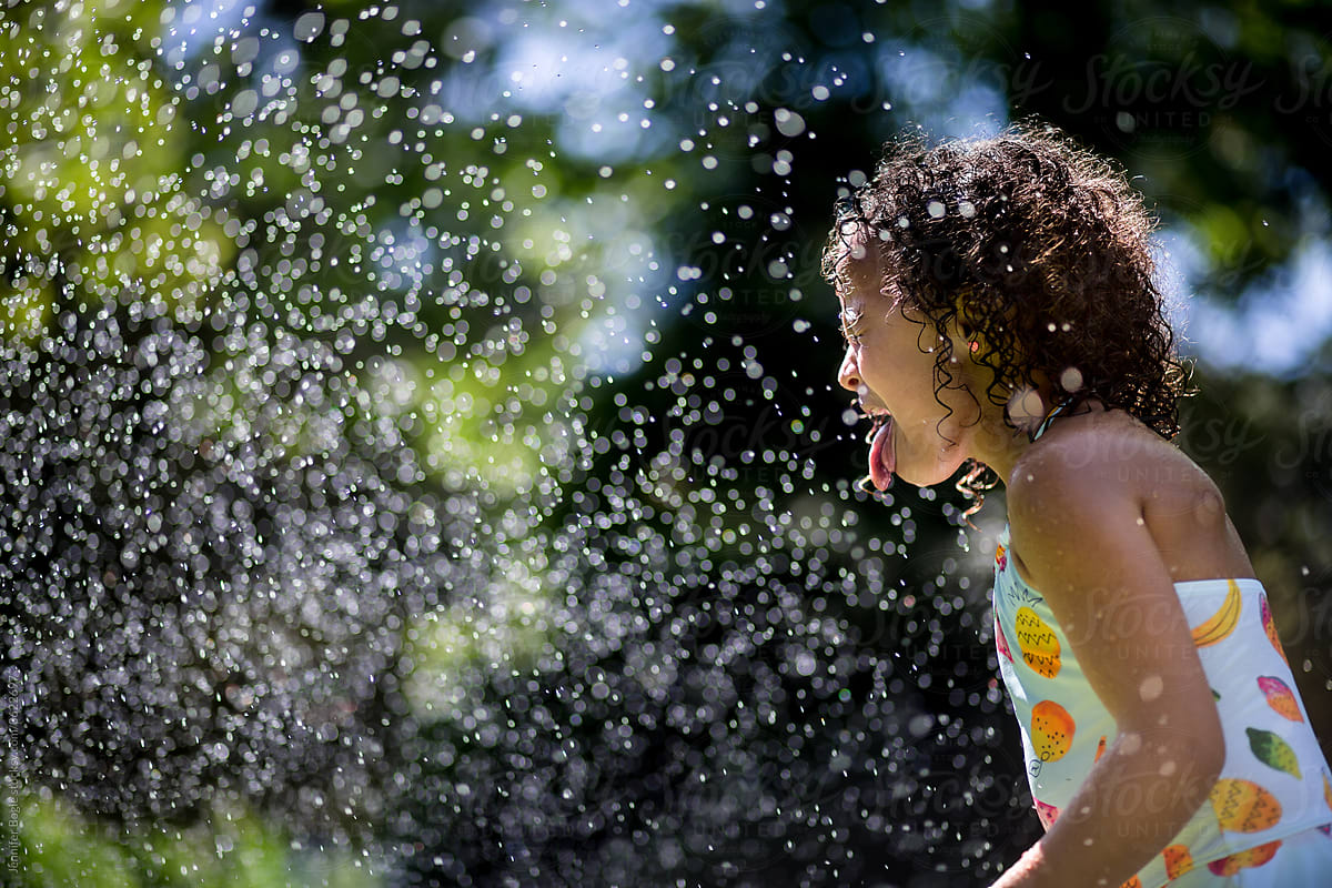 Girl in swimsuit catches water spray on her tongue