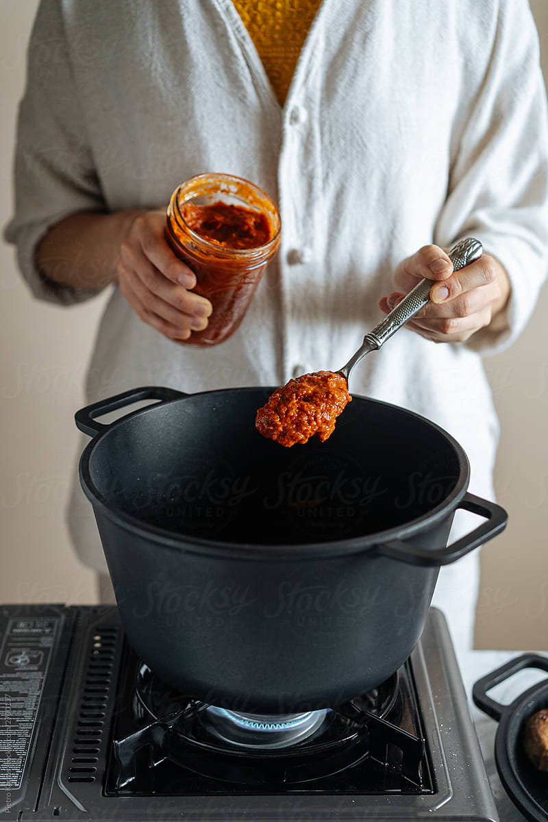 Faceless chef adding sauce in black pot on stove