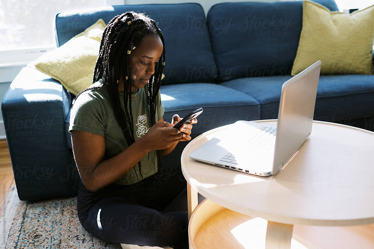 smiling black woman sitting in living room while using her phone