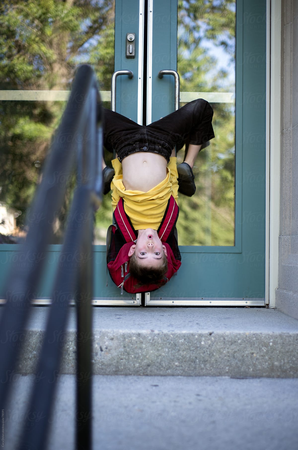 Silly Child Hangs Upside Down On The Doors Of A School by Cara Dolan