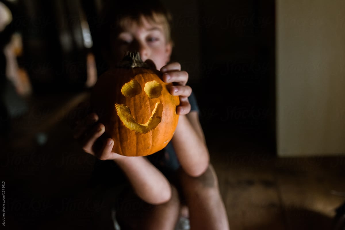 happy little boy holding a smiling pumpkin