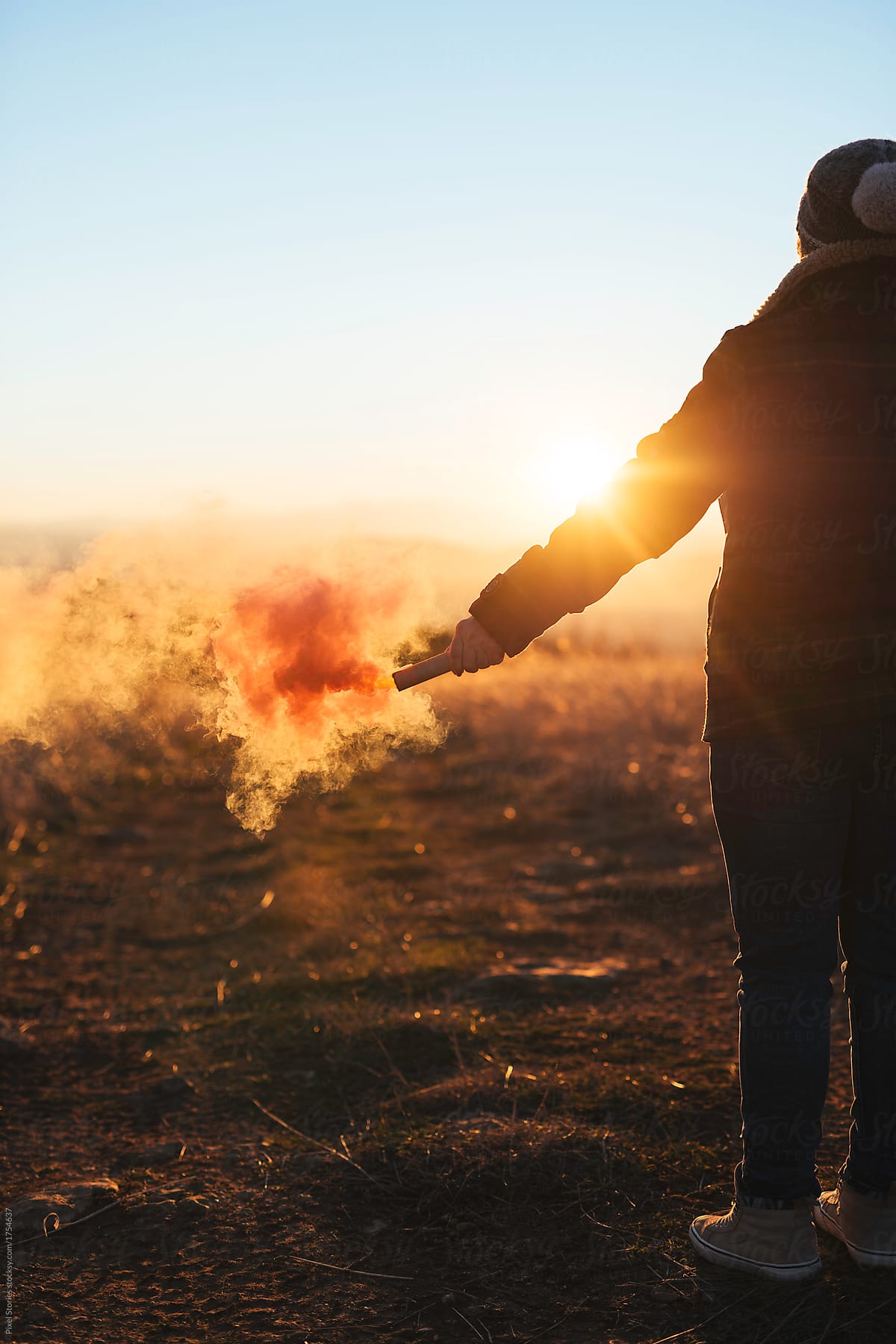 Woman holding colorful smoke bomb against the setting sun