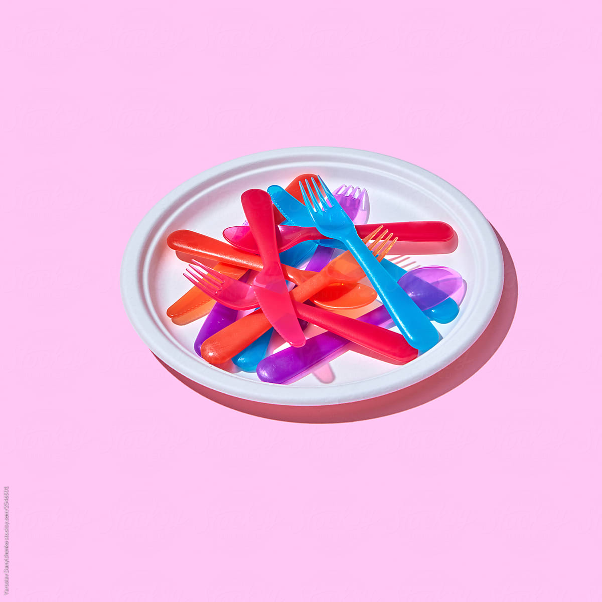 Plastic plate with knives, forks and spoons on a pink background