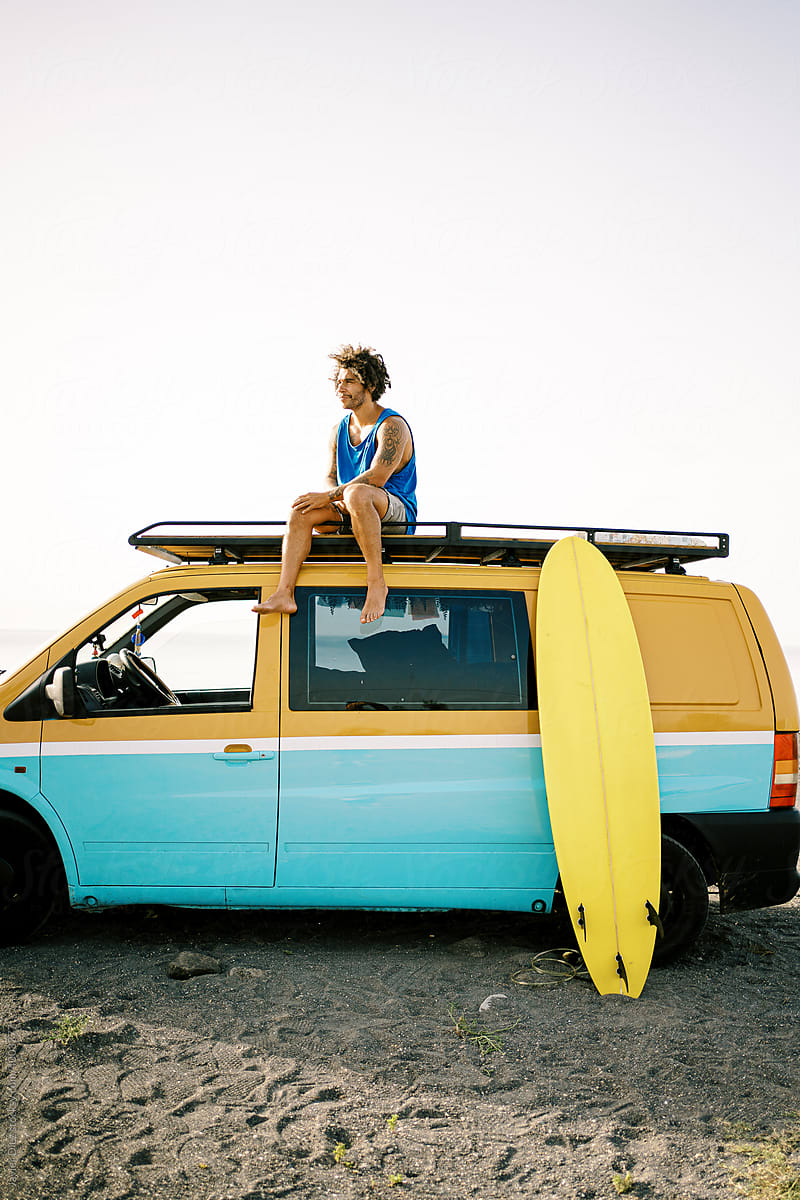 Travelling man with surfboard sitting on van