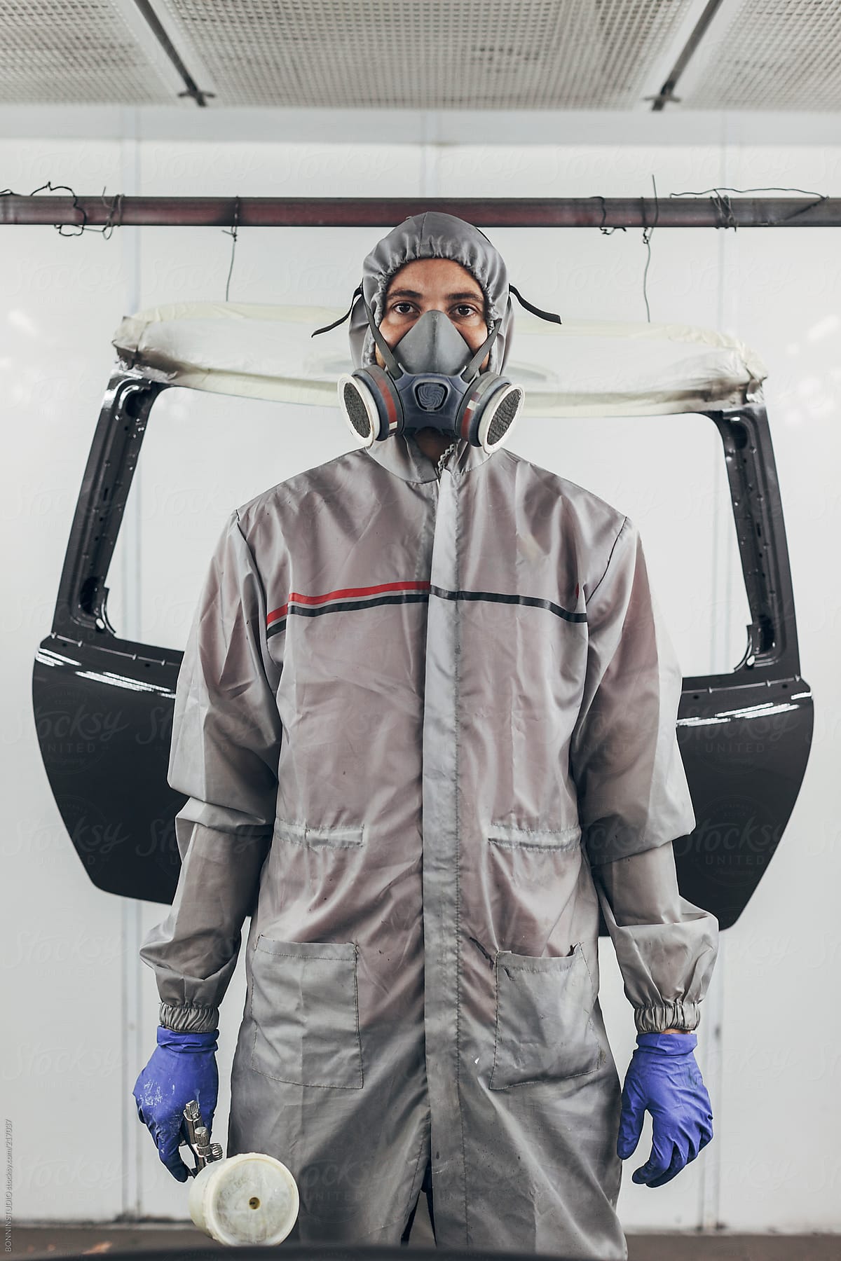 Portrait of a painter with mask working and painting pieces of a car in paint garage.