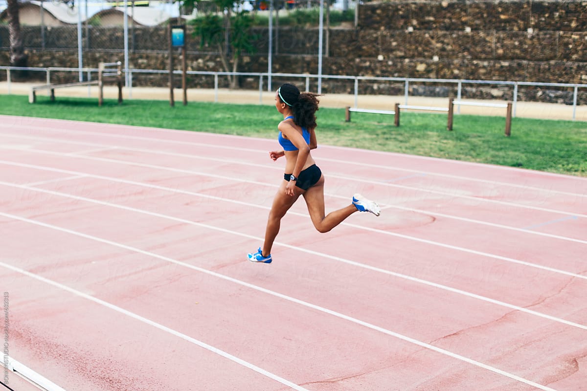 Back view of an african american female sprinter running on an athletics track.