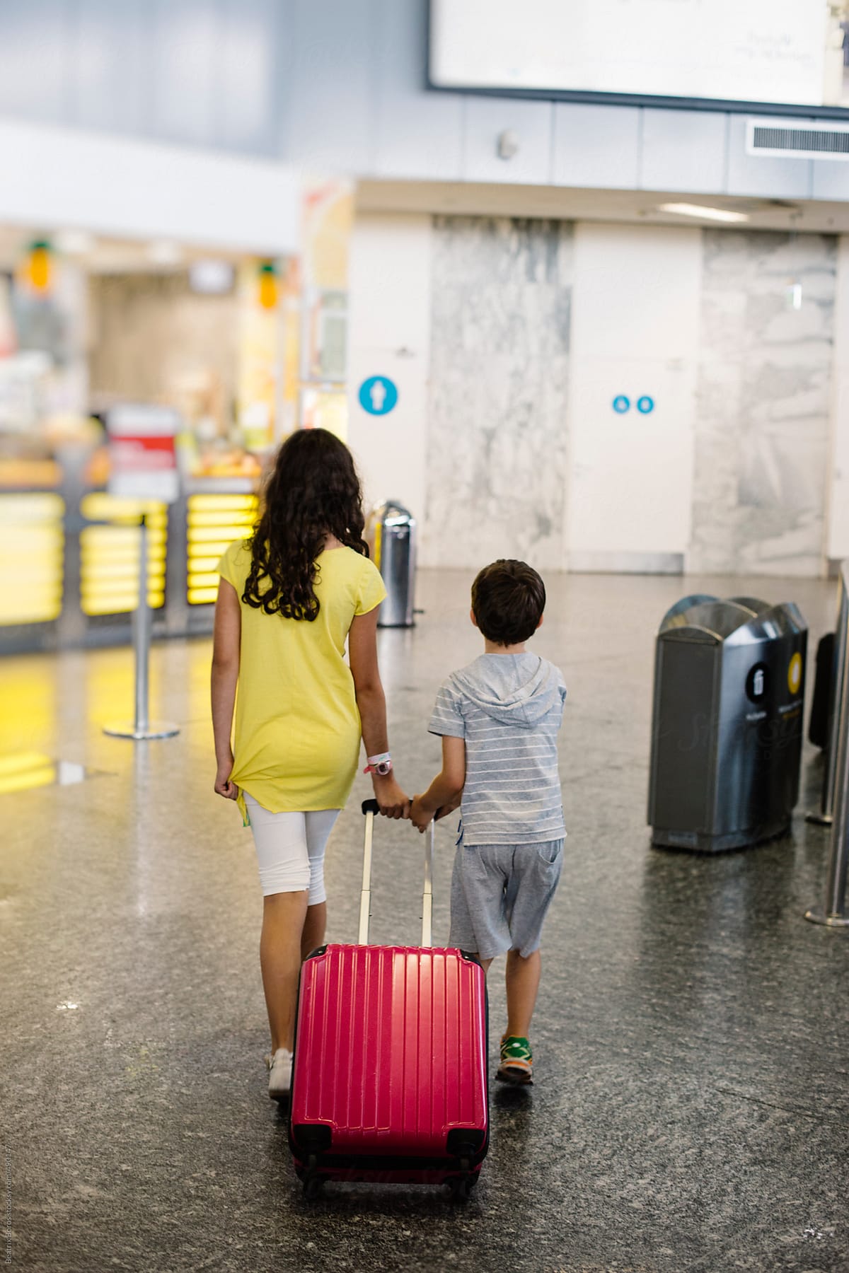 Siblings  walk away pulling together a pink luggage at the airport