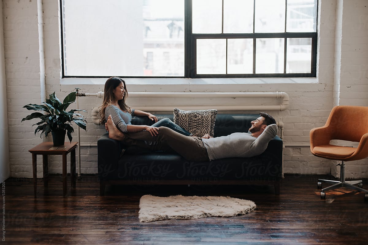 Attractive Young Interracial Couple Cuddling On Couch In Trendy Loft Apartment By Stocksy