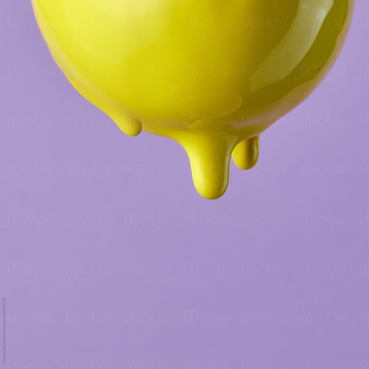 Close-up of a drop of yellow paint dripping from a pear on a purple background